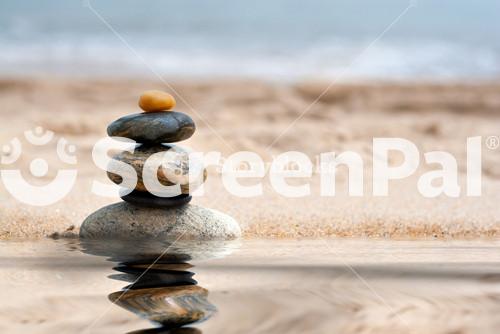 A Pile Of Round Smooth Zen Like Stones Stacked In The Sand At The Beach With A Mirror Reflection From A Pool Of Water.